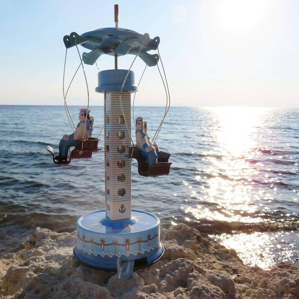 Von Hand aufgezogenes Blechkarussell Matrosen – Altmodisches Spielzeug aus vergangenen Tagen an einem sonnigen Strand